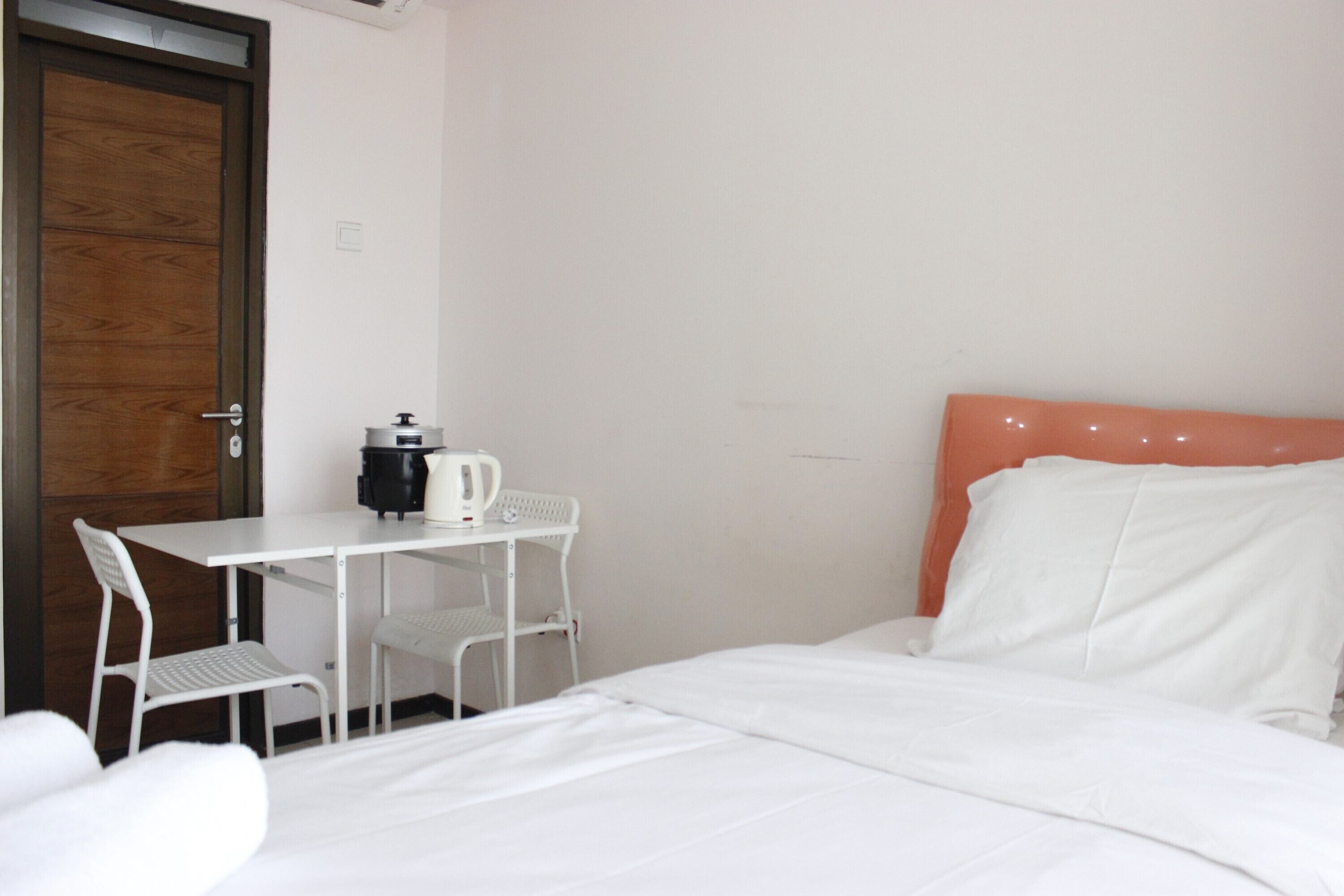 A hotel room with a bed, a white table with a kettle, and a chair.