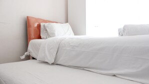 A hotel room with two beds, one with a white bedspread and the other with a white and orange headboard. - Cozy & Trendy Studio at Gateway Pasteur Apartment (Cimahi)