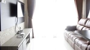 A modern living room with a flat-screen TV mounted on the wall, a leather sofa, and a wooden coffee table. - Elegant 2BR Gateway Pasteur Apartment near Exit Toll Pasteur (Cimahi)