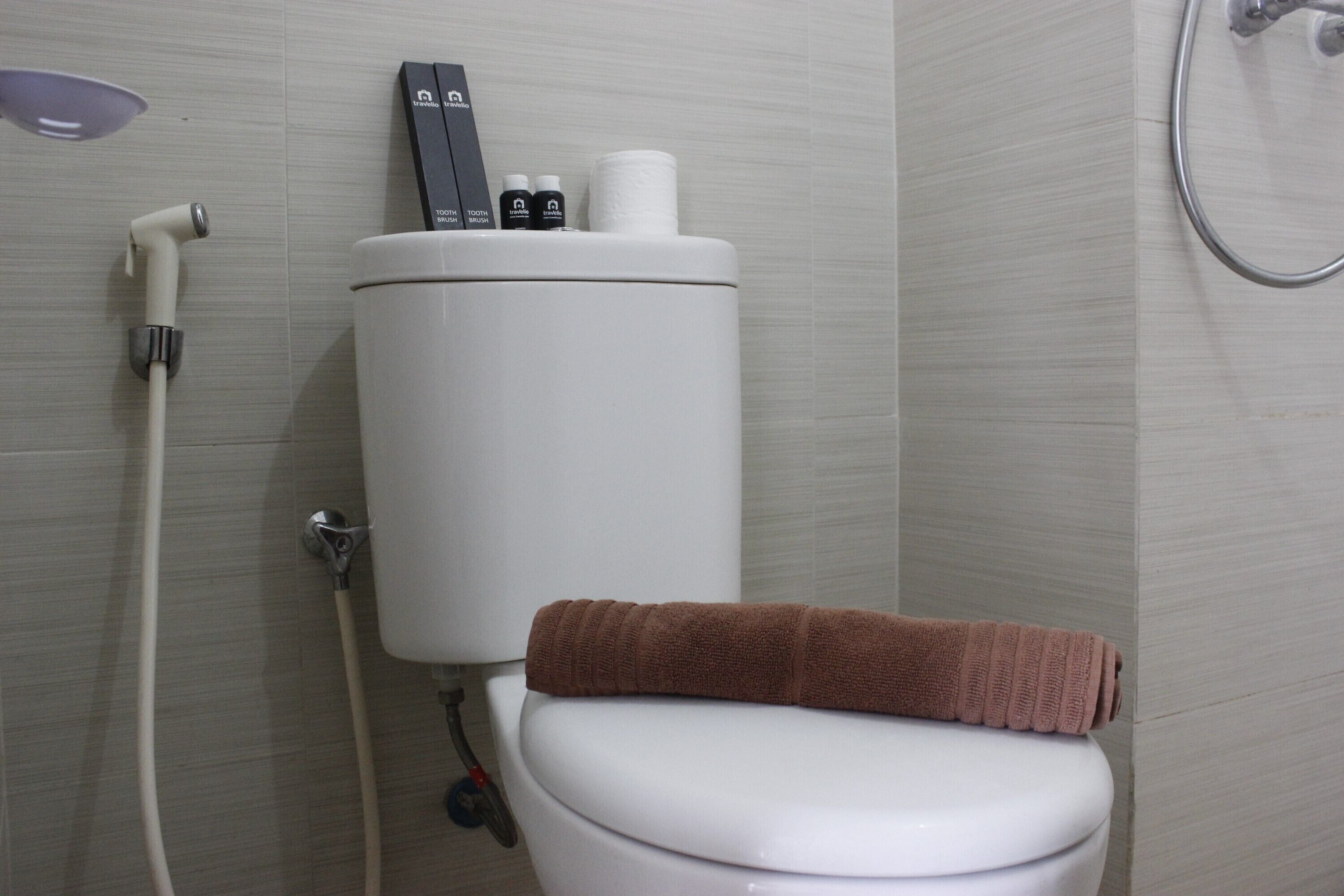 Une salle de bain avec des toilettes, un porte-rouleau de papier toilette blanc et une serviette posée sur la lunette des toilettes.