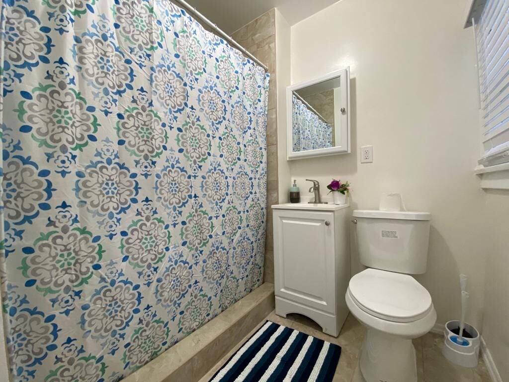 Een badkamer met een gordijn met een patroon, een toilet, een kastje, een spiegel en een gestreept vloerkleed.