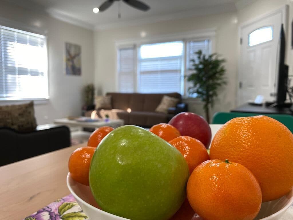 Ein Wohnzimmer mit einem Esstisch im Vordergrund, einer Couch und einem Fernseher im Hintergrund.