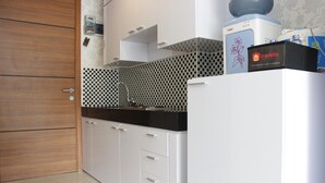 A modern kitchen with white cabinets, a black countertop, and a coffee machine. - Relaxing Studio near ITB at Beverly Dago Apartment (Bandung)