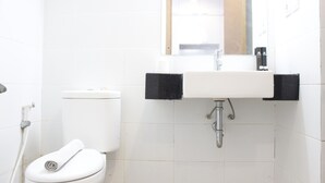 A bathroom with a white toilet, a sink with a mirror above it, and a black towel holder. - Relaxing Studio near ITB at Beverly Dago Apartment (Bandung)