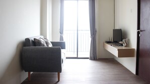 Un salón moderno con un sofá gris, un televisor de pantalla plana en un estante y un ventanal con cortinas.