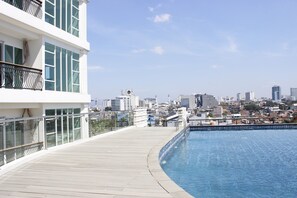 Une piscine sur le toit offrant une vue sur la ville, une balustrade en verre et un bâtiment moderne doté de balcons.