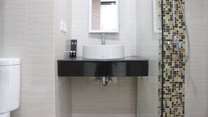 A bathroom with a white toilet, a black sink with a mirror above it, and a shower with mosaic tiles. - Strategic Studio at Green Kosambi Bandung Apartment (Bandung)
