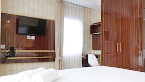 Una habitación de hotel con cama, televisión montada en la pared, escritorio con silla y armario.