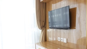 Una habitación moderna con un mueble de televisión de madera, un televisor de pantalla plana montado en la pared y una ventana con cortinas ligeras.