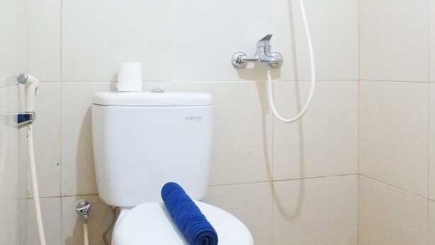 Un baño pequeño y blanco con un inodoro, una ducha y un rollo de toallas azules.