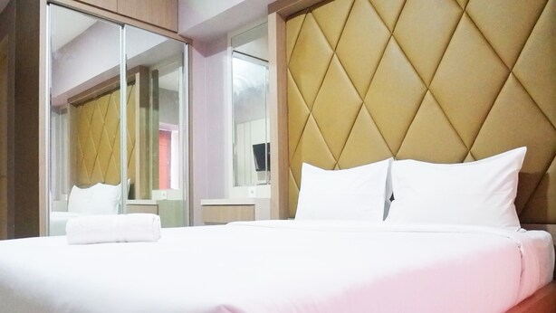A hotel room with a large bed, a tufted headboard, a mirror, and a wardrobe. - Minimalist Studio Apartment at Supermall Mansion Orchard (Surabaya)