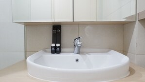 A bathroom with a white sink, a faucet, and two bottles of toiletries. - Minimalist Studio Apartment at Supermall Mansion Orchard (Surabaya)