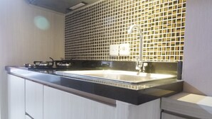 A modern kitchen with a black countertop, stainless steel appliances, and a tiled backsplash. - Minimalist Studio Apartment at Supermall Mansion Orchard (Surabaya)
