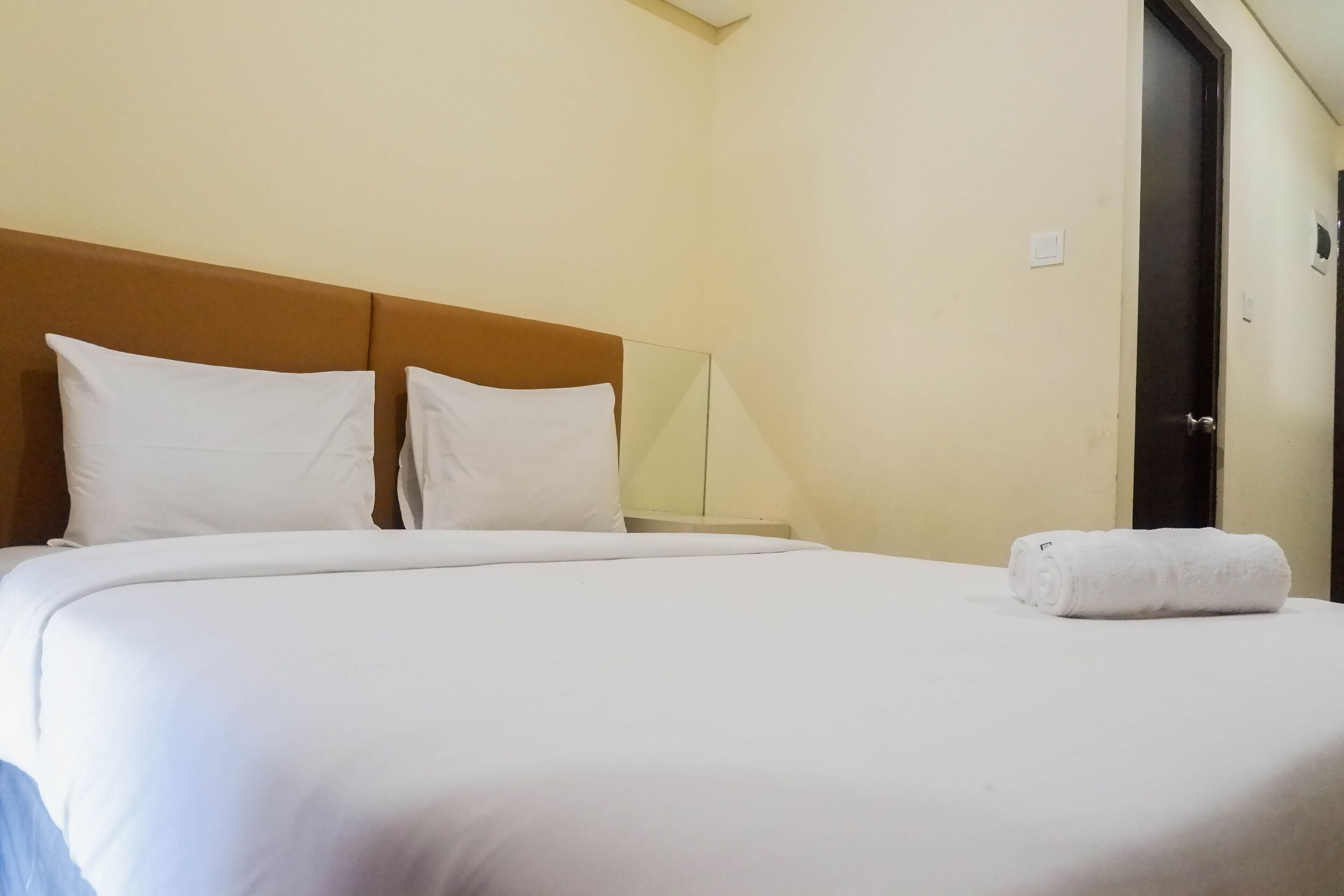 Cama bem arrumada com lençóis e almofadas brancos, cabeceira de madeira e uma toalha enrolada sobre a cama.