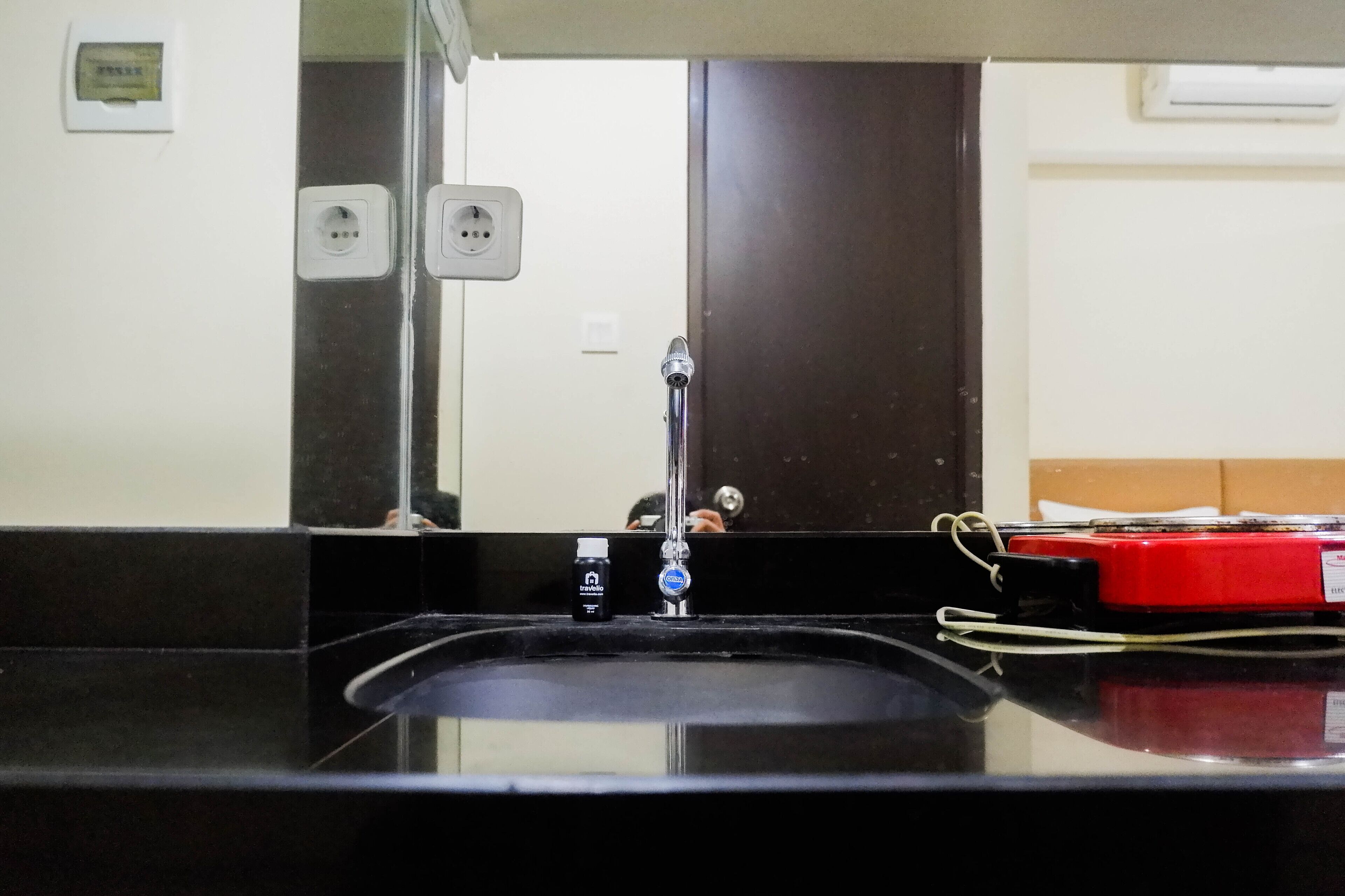 A bathroom sink with a mirror, a faucet, and a red device on the counter.