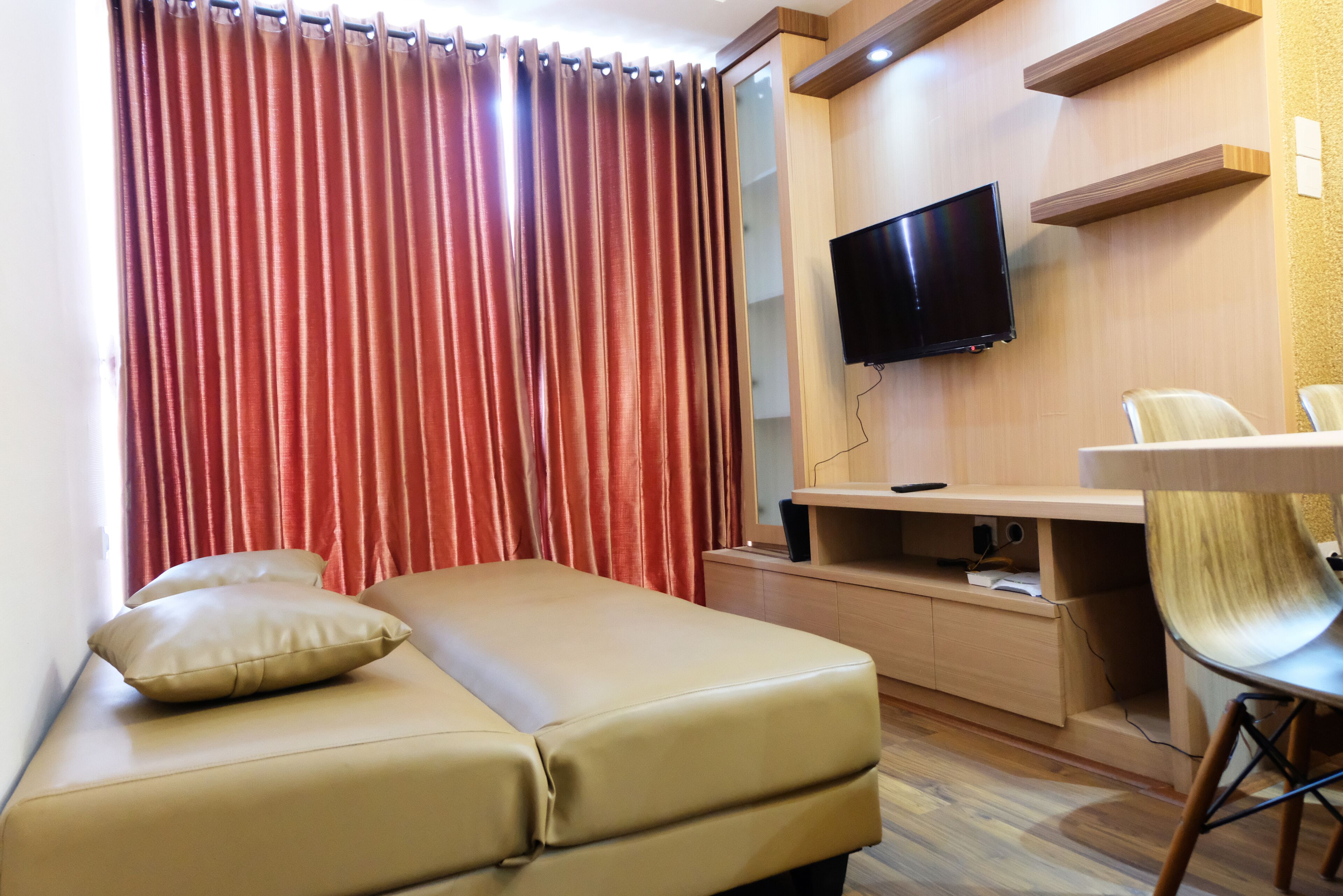 Ein modernes Zimmer mit einer Couch, einem an der Wand montierten Fernseher und einem Schreibtisch mit Stuhl.