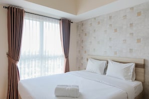 A hotel room with a large bed, white bedding, and a view of the city through sheer curtains.