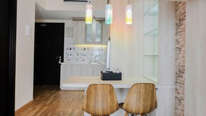 A modern kitchen with wooden cabinets, a countertop, and a built-in oven. There are two wooden chairs and a small table in front of the kitchen. - Comfy 1BR Apartment Casa De Parco Central BSD City (Pagedangan)
