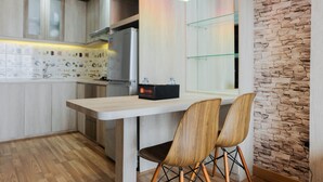 A modern kitchen with wooden cabinets, a white countertop, and two wooden chairs. - Comfy 1BR Apartment Casa De Parco Central BSD City (Pagedangan)