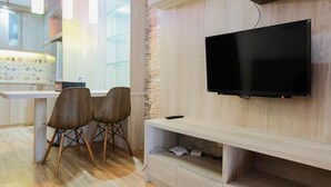 A modern kitchen with a built-in TV, wooden cabinets, and a dining area with chairs. - Comfy 1BR Apartment Casa De Parco Central BSD City (Pagedangan)