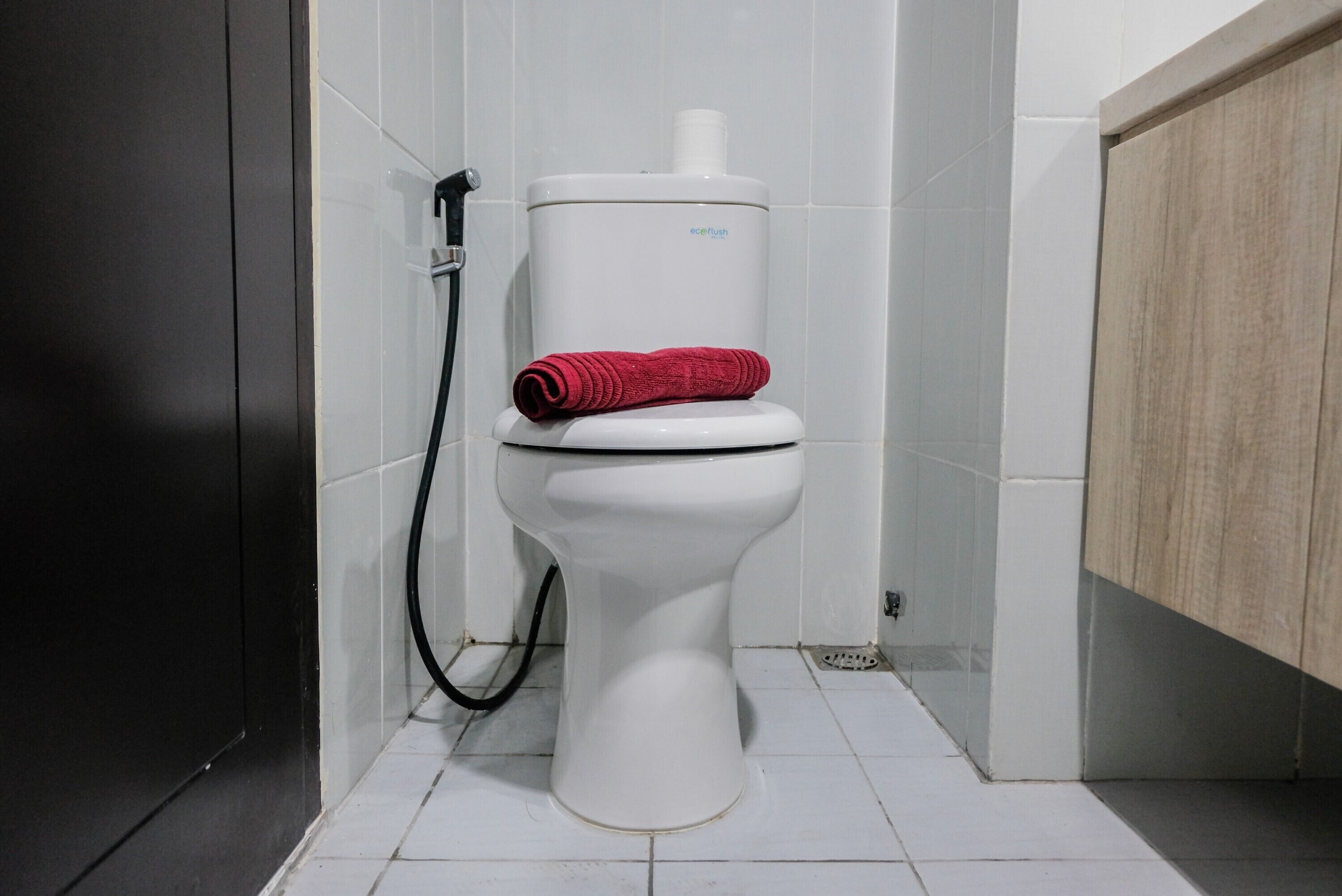 A white toilet with a red towel on top, a black hose, and a white tank.