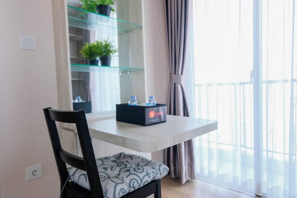 A dining area with a table, chairs, a glass shelf with plants, and a view of the outside through a window.