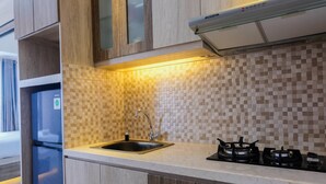 A modern kitchen with a tiled backsplash, a stainless steel sink, a gas stove, and wooden cabinetry. - Cozy and Luxurious Studio Casa de Parco Apartment (Pagedangan)