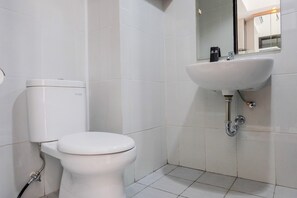 A bathroom with a toilet, sink, and mirror. - Homey and Comfy Studio Casa De Parco Apartment (Pagedangan)