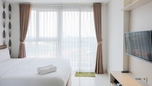 Una moderna camera d'hotel con un grande letto, una TV a schermo piatto e vista sulla città tramite tende trasparenti.