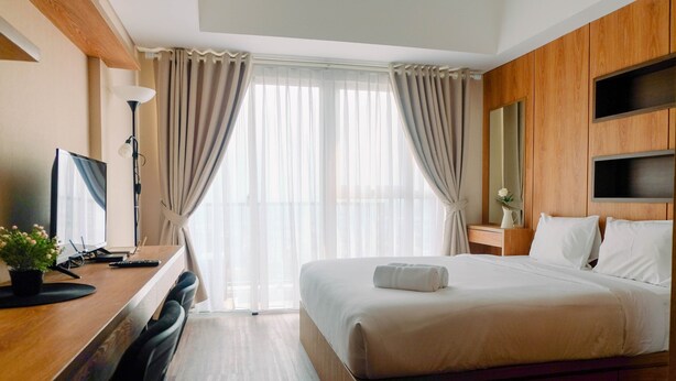 A hotel room with a bed, a desk with a computer, a chair, a lamp, and a window with curtains.