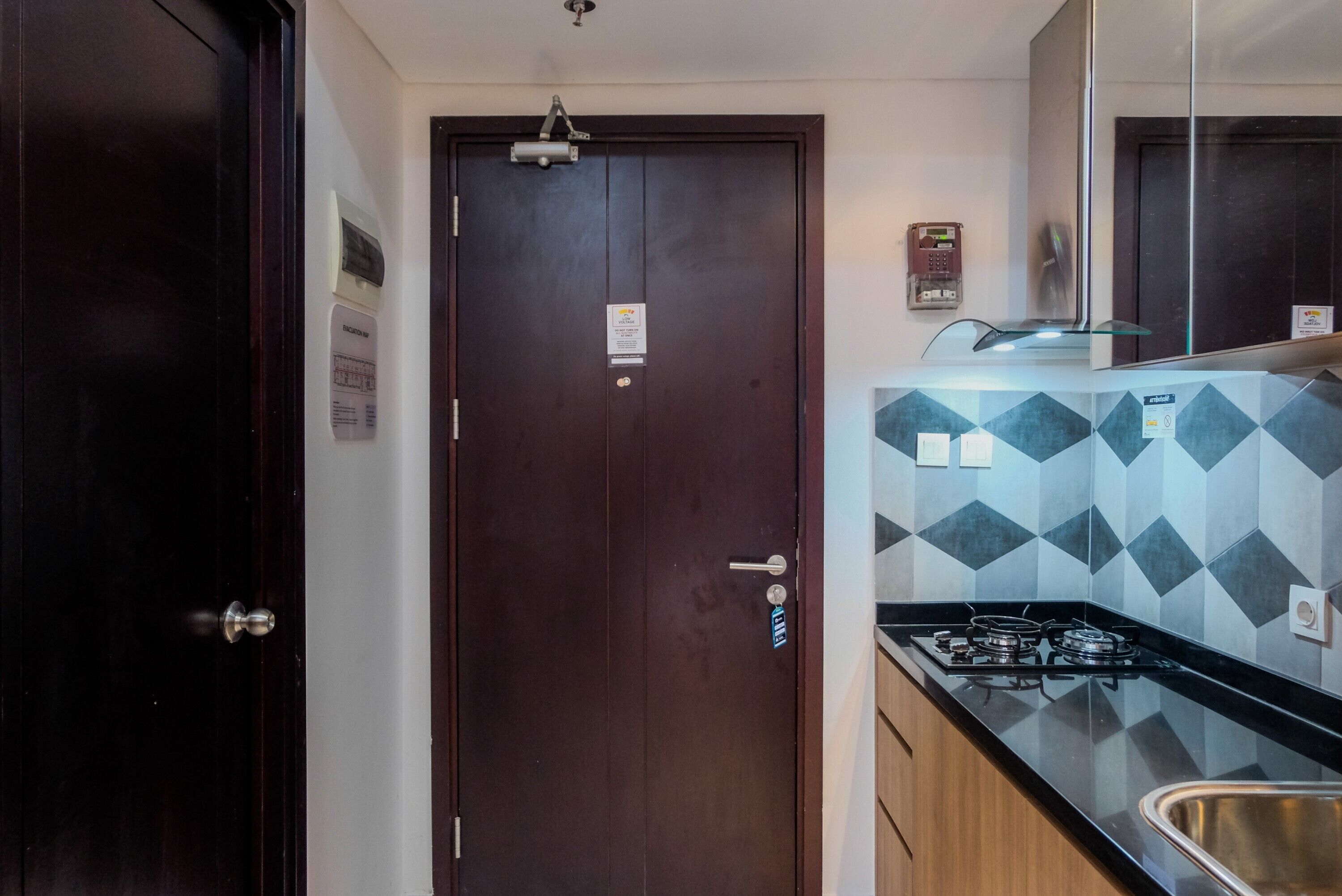 A narrow hallway with a dark wooden door, a tiled backsplash with a geometric pattern, and a stainless steel sink.