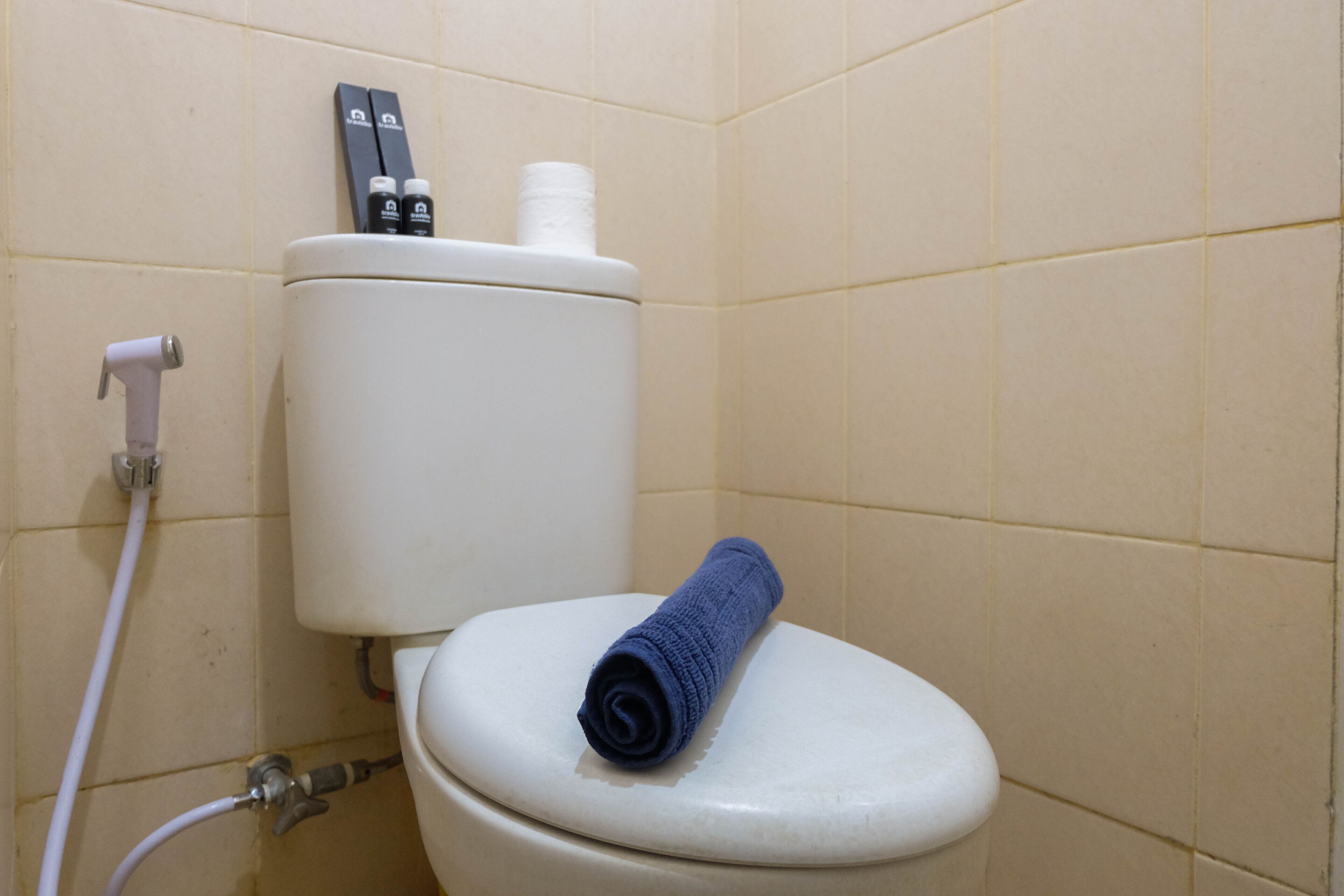 A toilet with a blue towel on the seat, a toilet paper holder, and a bidet spray.
