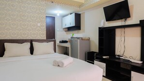 A hotel room with a bed, a desk, a television, and a kitchenette. - Fully Furnished Studio at Serpong Greenview Apartment (South Tangerang)
