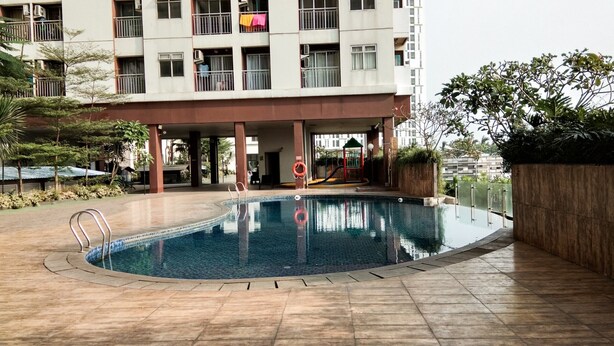 A swimming pool with a tiled deck, a children's play area, and a multi-story building with balconies in the background. - Fully Furnished Studio at Serpong Greenview Apartment (South Tangerang)