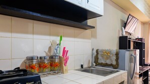 A kitchen with a gas stove, a sink, and a refrigerator. There are jars with flowers and kitchen utensils on the counter. - Fully Furnished Studio at Serpong Greenview Apartment (South Tangerang)