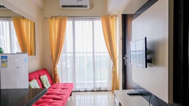 Ein Hotelzimmer mit einem roten Sofa, einem Flachbildfernseher, einer kleinen Küchenzeile und einem Balkon mit gelben Vorhängen.