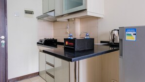 Eine Küche mit schwarzem Arbeitsplatz, einer Mikrowelle, einem Wasserkocher und einem Kühlschrank.