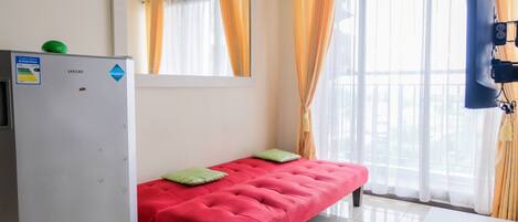 A room with a red bed, a white wall, a mirror, and a window with curtains.