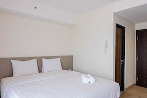 A neatly made bed with white linens and two rolled towels, a wooden headboard, and a door to the right. - Highest Value Studio Room at Annora Living Apartment (Tangerang)