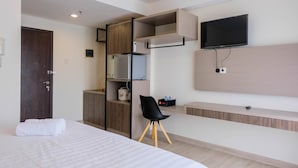 A modern hotel room with a bed, a desk, a chair, a TV, and built-in storage. - Highest Value Studio Room at Annora Living Apartment (Tangerang)