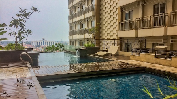 A rooftop swimming pool with a waterfall feature, surrounded by lounge chairs and potted plants. - Highest Value Studio Room at Annora Living Apartment (Tangerang)