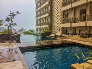 A rooftop swimming pool with a waterfall feature, surrounded by lounge chairs and potted plants. - Highest Value Studio Room at Annora Living Apartment (Tangerang)