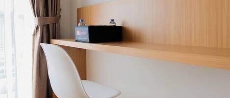 Habitación de hotel con estante de madera, una silla blanca y un minibar.