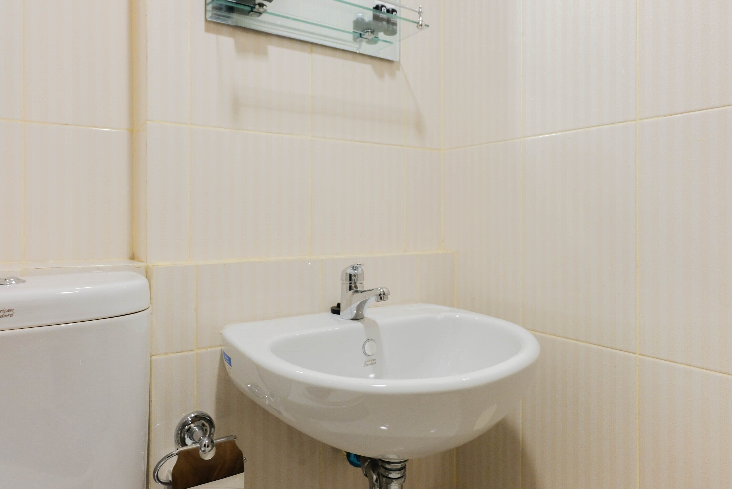 A bathroom with a white sink, a toilet, and a glass shelf above the sink.