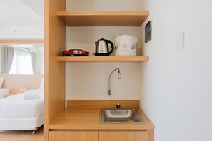 A compact kitchenette with a stainless steel sink, a kettle, and a slow cooker on a wooden shelf. - Twin Bed Studio Room at Annora Living Apartment (Tangerang)