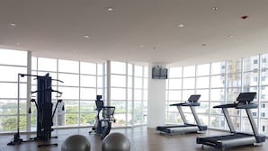 A spacious gym with large windows, a variety of exercise equipment, and a wooden floor. - Cozy Studio Apartment at Tree Park City (Tangerang)