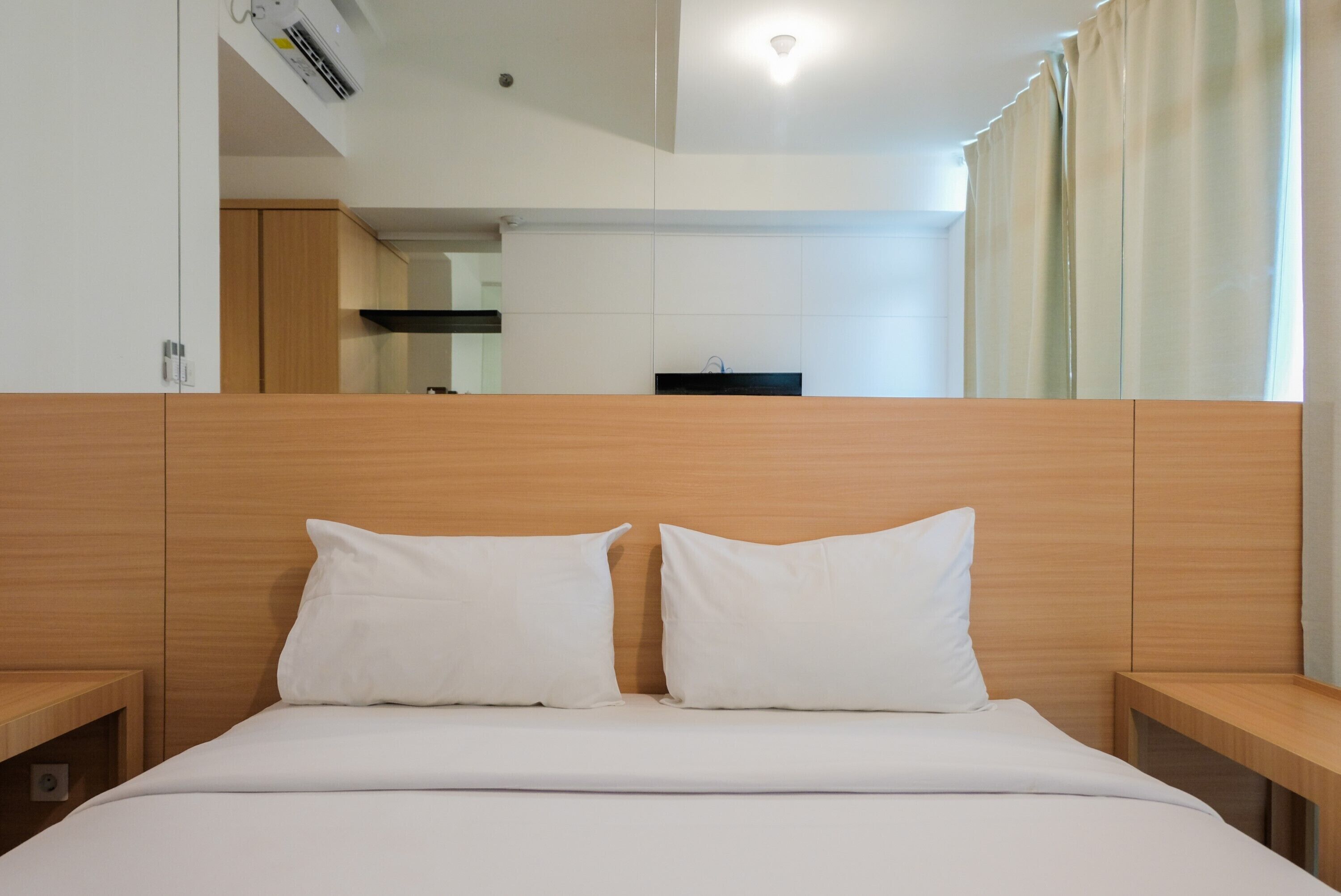 Een hotelkamer met een houten hoofdeinde, een bed met witte lakens en een uitzicht op de keuken door een spiegel.