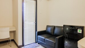 Una habitación pequeña y moderna con un sofá de cuero negro, un escritorio blanco y un televisor Sharp negro.