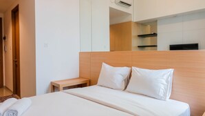 A hotel room with a bed, a wooden headboard, a nightstand, a mirror, and a wall-mounted air conditioning unit. - Simply and Homey Studio Apartment at Tree Park City (Tangerang)