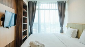 Hotellihuone, jossa on sänky, seinälle asennettu televisio, ikkuna verhoilla ja näkymä ulos.